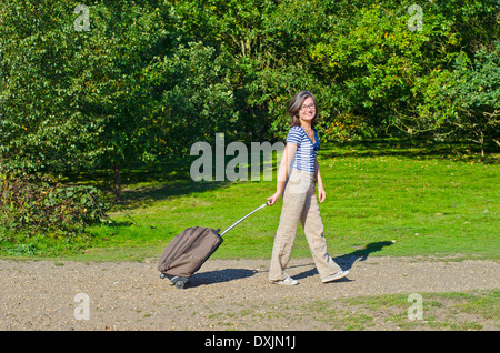woman walking though park pulling roller case Stock Photo