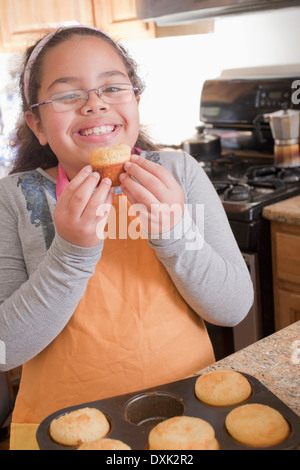 Portrait of smiling Hispanic girl eating muffin in kitchen Stock Photo