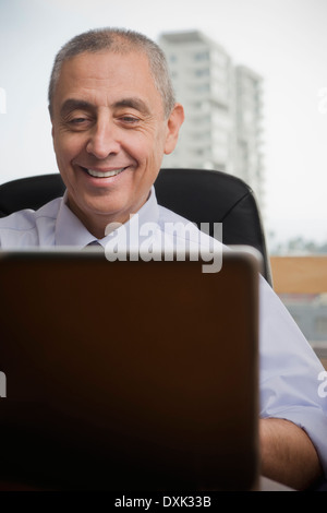 Close up of smiling Hispanic businessman using laptop Stock Photo