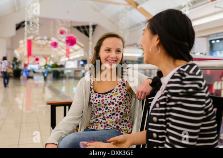 Girls talking on bench at shopping mall Stock Photo