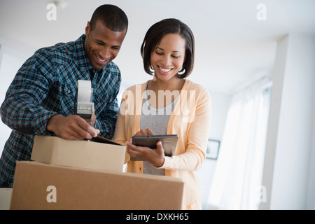Couple with digital tablet taping up moving boxes Stock Photo
