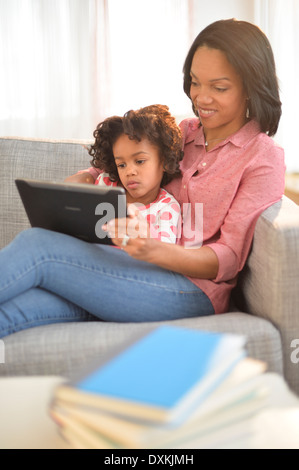 Black mother and daughter using digital tablet on sofa Stock Photo