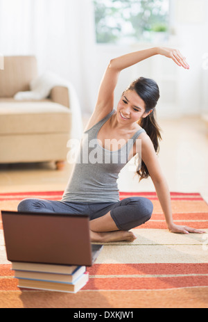 Hispanic woman on rug stretching in front of laptop Stock Photo