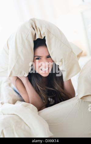 Portrait of frustrated Hispanic woman under pillow in bed Stock Photo