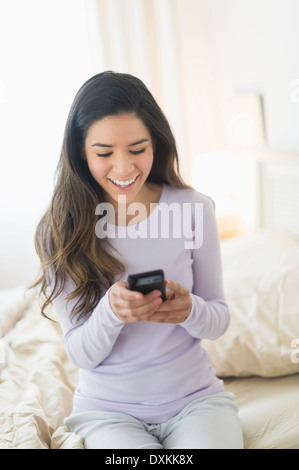 Happy Hispanic woman text messaging in bed Stock Photo