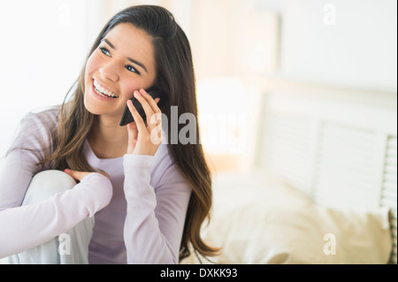 Happy Hispanic woman talking on cell phone in bed Stock Photo