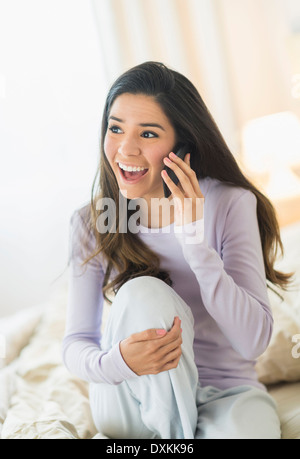 Enthusiastic Hispanic woman talking on cell phone in bed Stock Photo