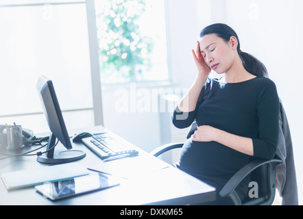 Tired pregnant Japanese businesswoman at desk Stock Photo