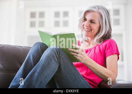 Happy Caucasian woman reading book on sofa Stock Photo