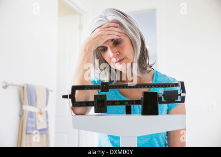 Unhappy Caucasian woman standing on weight scale Stock Photo