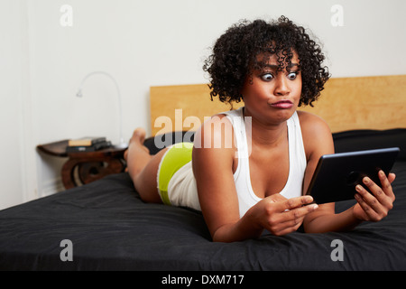 Mixed race woman using digital tablet on bed Stock Photo