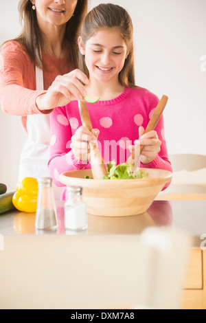Caucasian mother and daughter tossing salad in kitchen