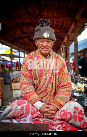 Bhutanese man in traditonal national dress and wearing a woolen hat with a badge depicting King Jigme Dorji Wangchuk sitting in Stock Photo