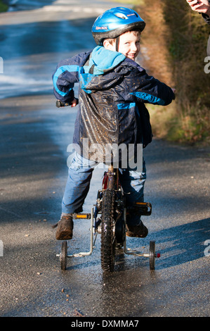 Boy sitting on bike after cycling through muddy puddles Stock Photo