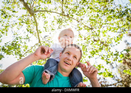 Cute Young Boy Rides Piggyback On His Dads Shoulders Outside at the Park. Stock Photo