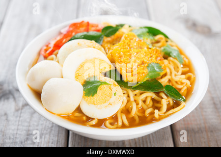 Spicy curry instant noodles soup on wooden dining table. Fresh cooked, hot with steamed smoke. Stock Photo