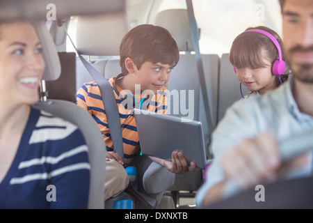 Brother and sister sharing digital tablet in back seat of car Stock Photo