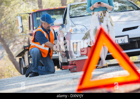 Roadside mechanic changing tire behind warning triangle Stock Photo