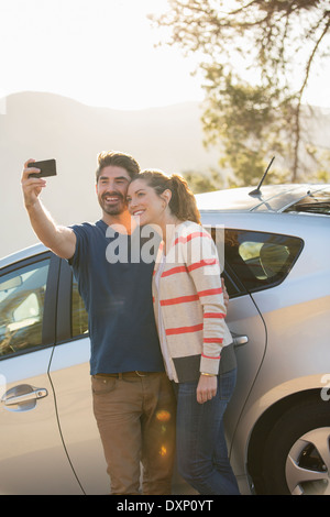 Couple taking self-portrait with camera phone outside car Stock Photo
