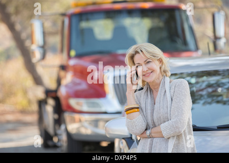 Woman talking on cell phone near tow truck at roadside Stock Photo