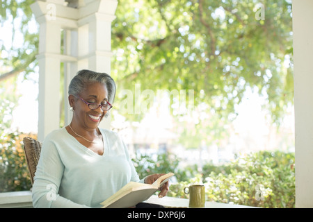 Happy senior woman reading book on porch Stock Photo