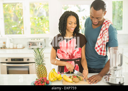 Couple slicing fruit next to blender in kitchen Stock Photo