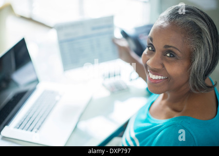 Portrait of smiling woman paying bills at laptop Stock Photo