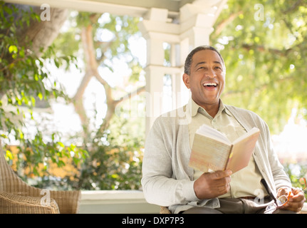 Laughing senior man reading book on porch Stock Photo