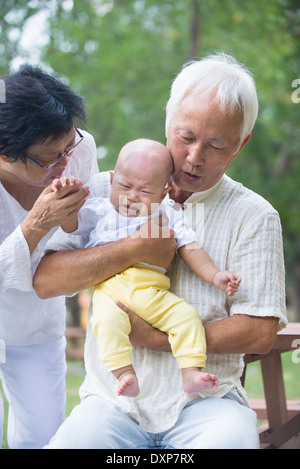 asian baby crying while being comforted by grandparents Stock Photo