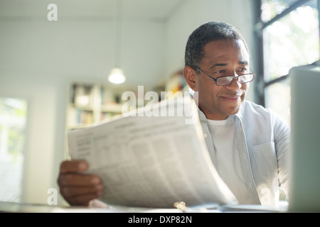 Senior man with newspaper using laptop Stock Photo