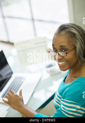 Portrait of smiling senior woman paying bills at laptop Stock Photo