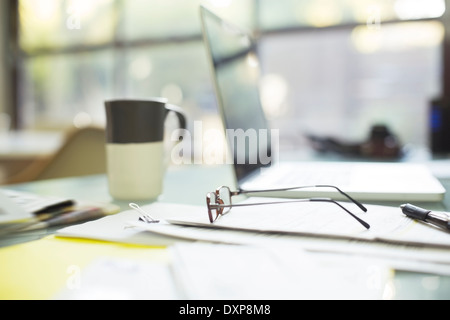 Close up of coffee cup and eyeglasses on paperwork near laptop Stock Photo