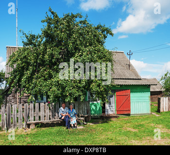 Mother and son sitting on a bench near the village house. Stock Photo