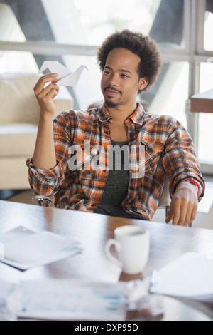 Pensive creative businessman looking at origami swan in office Stock Photo