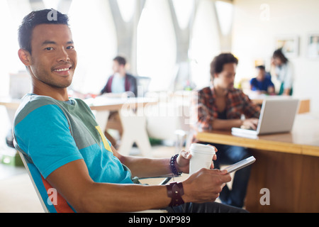 Portrait of smiling casual businessman drinking coffee and using digital tablet in office Stock Photo