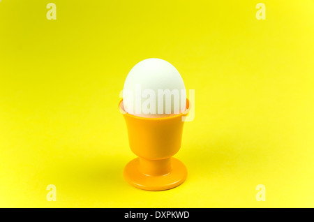 Single egg in a yellow egg cup at yellow background Stock Photo