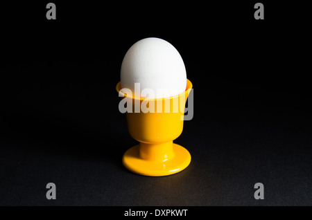 Single egg in a yellow egg cup at black background Stock Photo
