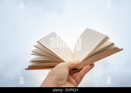 Open book in female hand on a background of sky Stock Photo