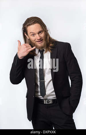 A bearded long hair man in suit holding up his hand gesturing a phone call. A humorous portrait concept Stock Photo