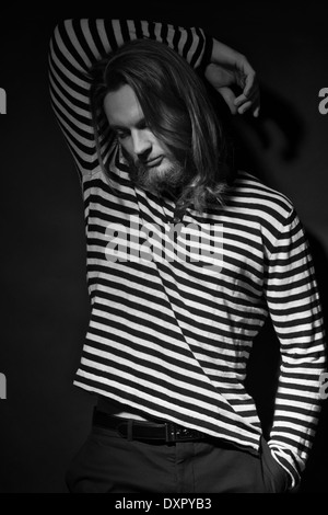 A beaded man, long hair, male model, posing in a stripe shirt. A dark black and white men's fashion portrait Stock Photo