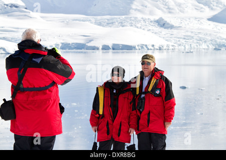 Antarctica tourists on cruise pose for camera in front of beautiful Antarctic landscape of glacier and iceberg. Stock Photo
