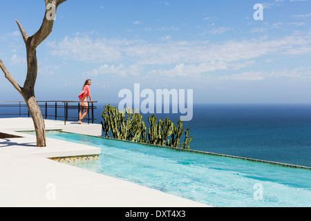 Woman standing on poolside balcony overlooking ocean Stock Photo