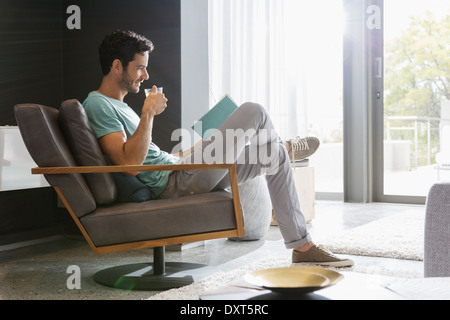 Man drinking tea and reading book in living room Stock Photo