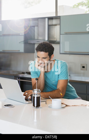 Man drinking coffee and using laptop in kitchen Stock Photo