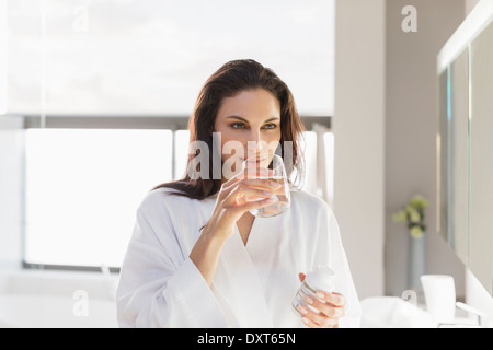 Woman taking medication with water in bathroom Stock Photo
