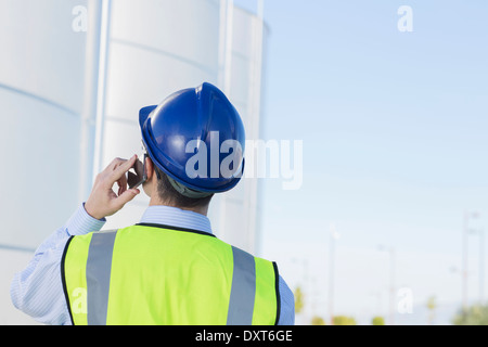 Worker talking on cell phone and looking up at silage storage towers Stock Photo