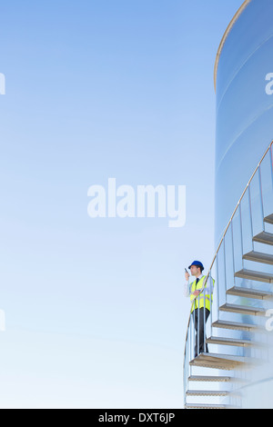 Worker using walkie-talkie on winding steps along silage storage tower Stock Photo
