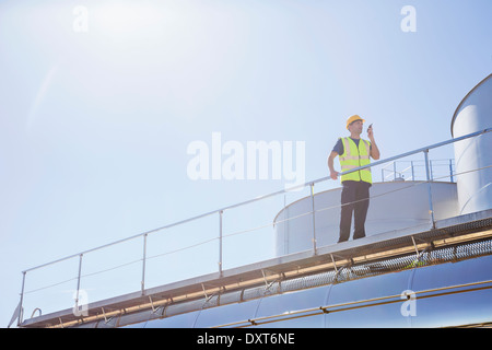 Worker using walkie-talkie on platform next to silage storage towers Stock Photo