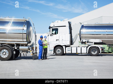 Workers talking next to stainless steel milk tankers Stock Photo