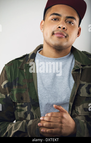 Closeup portrait of young man in casuals. Young male model wearing camouflage jacket and cap on gray background Stock Photo